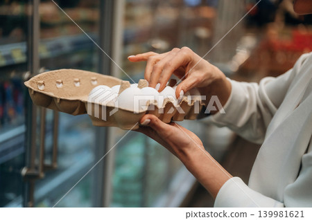 Woman selecting fresh eggs from a carton in a grocery store, showcasing the importance of quality food choices and healthy eating habits in daily life Woman selecting fresh eggs from a carton in a grocery store, showcasing the importance of quality food choices and healthy eating habits in daily life 139981621