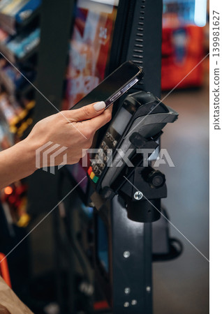 Hand holding smartphone near contactless payment terminal in a vending machine environment, showcasing modern technology and convenience in transactions 139981627