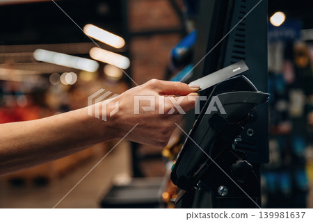 Hand of a customer holding a credit card near a payment terminal in a retail store, showcasing the transaction process in a modern shopping environment 139981637