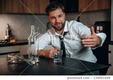 Smiling man in a white shirt and tie gestures while sitting at a kitchen table with a glass and a bottle, conveying a relaxed atmosphere around alcohol consumption Smiling man in a white shirt and tie gestures while sitting at a kitchen table with a glass and a bottle, conveying a relaxed atmosphere around alcohol consumption 139981898