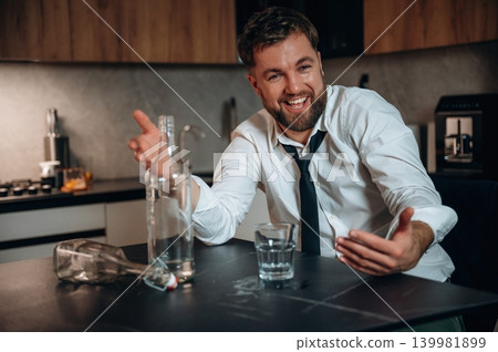 Smiling man in a white shirt and tie gestures animatedly at a table with a glass and bottle, conveying a lively atmosphere of celebration and enjoyment 139981899