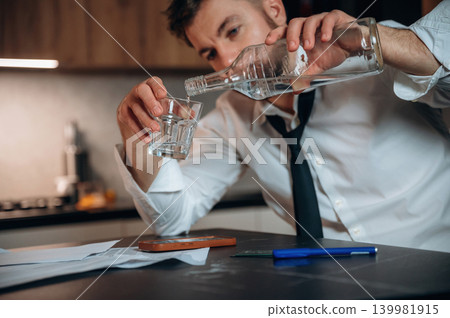 Man in white shirt and black tie pouring alcohol into a glass while sitting at a table with papers, creating a contemplative atmosphere of relaxation and indulgence Man in white shirt and black tie pouring alcohol into a glass while sitting at a table with papers, creating a contemplative atmosphere of relaxation and indulgence 139981915