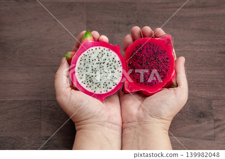 Freshly cut dragon fruit in a woman hands. Slices of delicious pitahaya fruit on wooden background Freshly cut dragon fruit in a woman hands. Slices of delicious pitahaya fruit on wooden background 139982048