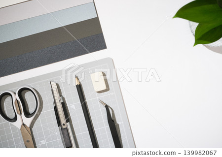 Flat lay of craft tools and stationery on a white desk. Grey cutting mat, scissors, utility knife, pencil, tweezers, and paper. Copyspace Flat lay of craft tools and stationery on a white desk. Grey cutting mat, scissors, utility knife, pencil, tweezers, and paper. Copyspace 139982067