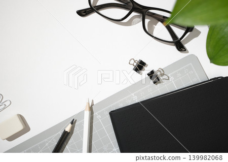 Office supplies on a white background. Black eyeglasses, pencils, eraser, binder clips, cutting mat, and notebook. Copyspace Office supplies on a white background. Black eyeglasses, pencils, eraser, binder clips, cutting mat, and notebook. Copyspace 139982068