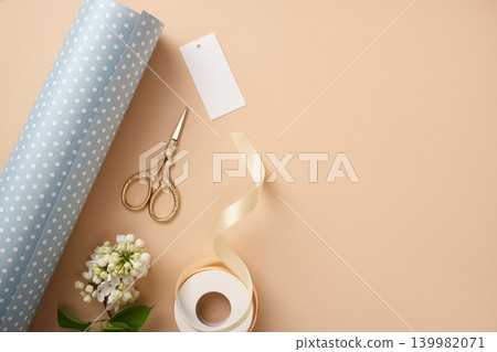 Gift wrapping supplies with pastel polka dot paper, ribbon, scissors, blank tag and white flowers on beige background. Copyspace Gift wrapping supplies with pastel polka dot paper, ribbon, scissors, blank tag and white flowers on beige background. Copyspace 139982071