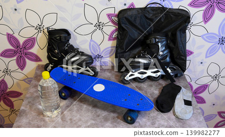 blue plastic skateboard and black roller skates with a water bottle on a table blue plastic skateboard and black roller skates with a water bottle on a table 139982277