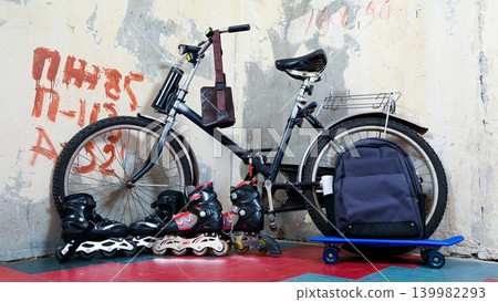 bicycle skateboard and roller skates near the wall bicycle skateboard and roller skates near the wall 139982293