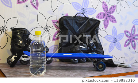 clear water bottle in front of a blue skateboard and black roller skates on a table clear water bottle in front of a blue skateboard and black roller skates on a table 139982310