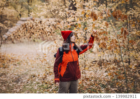 Woman stands in autumn forest holding oak branch with brown leaves. responsible nature tourism, low impact recreation, ecological footprint awareness, forest conservation support. Woman stands in autumn forest holding oak branch with brown leaves. responsible nature tourism, low impact recreation, ecological footprint awareness, forest conservation support. 139982911