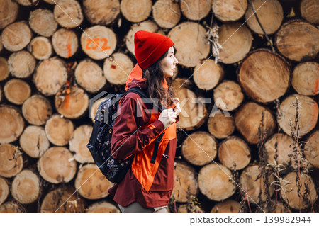 Woman walks past stacked timber logs in woodland area. Woman forest inspector, female industrial professional, environmental auditor at work. Woman walks past stacked timber logs in woodland area. Woman forest inspector, female industrial professional, environmental auditor at work. 139982944