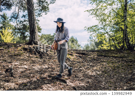 Woman walks along forest trail past large tree roots. Weekend getaway inspiration, micro adventure travel, exploring local nature. 139982949