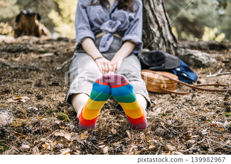 Feet wearing rainbow socks rest on forest ground while person sits in background. lgbtq mental health, queer mindfulness nature, finding inner peace, mental wellness awareness. 139982967