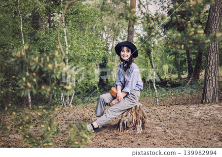 Person wearing hat sits on tree stump in forest and smiles while looking away. Modern forest explorer, weekend getaway activities, domestic tourism trend, Hiking leisure time. Person wearing hat sits on tree stump in forest and smiles while looking away. Modern forest explorer, weekend getaway activities, domestic tourism trend, Hiking leisure time. 139982994
