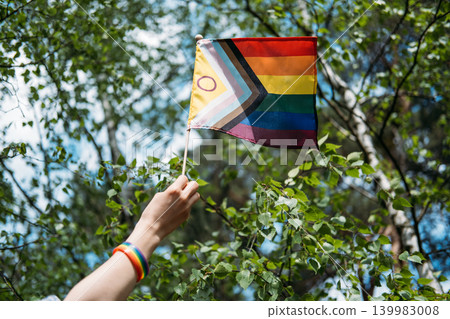 Hand holds inclusive pride flag toward sky. LGBTQ Identity, gender expression, authentic self, pride symbol. Hand holds inclusive pride flag toward sky. LGBTQ Identity, gender expression, authentic self, pride symbol. 139983008