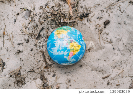 Small globe lies on dry sandy ground among debris. Global pollution problem, planet in danger, environmental degradation concept. Small globe lies on dry sandy ground among debris. Global pollution problem, planet in danger, environmental degradation concept. 139983029