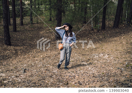 Young woman stands in forest while shielding eyes and looking into distance. Eco-conscious traveler, exploring local woods, appreciation of biodiversity. Young woman stands in forest while shielding eyes and looking into distance. Eco-conscious traveler, exploring local woods, appreciation of biodiversity. 139983040