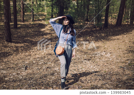 Woman stands on forest floor shielding eyes with hand while looking into distance. Exploring wilderness nearby, low cost travel ideas, authentic forest walk. Woman stands on forest floor shielding eyes with hand while looking into distance. Exploring wilderness nearby, low cost travel ideas, authentic forest walk. 139983045