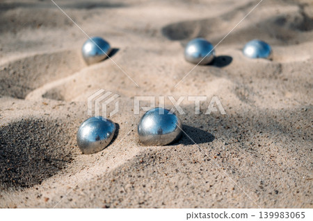 Metal spheres lie scattered on sandy surface in sunlight. petanque boules set, Beach resort activities, summer holiday entertainment, family vacation games. 139983065