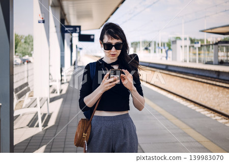 Woman stands on railway platform looking at smartphone. Solo female traveler, independent woman journey, female adventure seeker 139983070