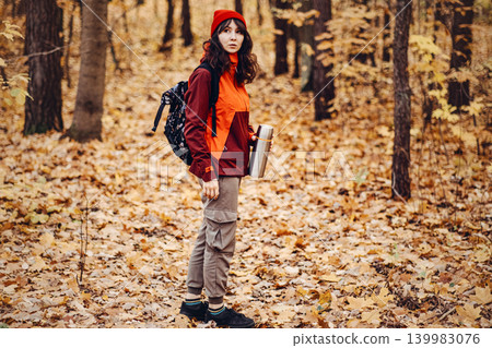 Woman stands in autumn forest holding thermos. wilderness survival skills, outdoor escape plan, off-grid living preparation. Woman stands in autumn forest holding thermos. wilderness survival skills, outdoor escape plan, off-grid living preparation. 139983076