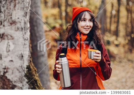 Smiling woman holds metal thermos and cup in autumn forest. Low carbon footprint, ethical travel choices, nature based wellness. Smiling woman holds metal thermos and cup in autumn forest. Low carbon footprint, ethical travel choices, nature based wellness. 139983081