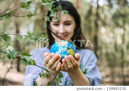 Smiling woman holds globe model in hands outdoors near tree branches. Ecology conservation efforts, green business initiative, protecting global ecosystem. 139983130
