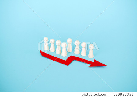 Line of wooden peg dolls stands behind red downward arrow on blue background. Corporate mass layoffs, rising unemployment rate, job market instability, Human resources crisis. Line of wooden peg dolls stands behind red downward arrow on blue background. Corporate mass layoffs, rising unemployment rate, job market instability, Human resources crisis. 139983355