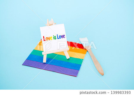 Miniature easel holds canvas with Love is Love text on rainbow flag next to paintbrush. inclusive art, pride month marketing, LGBTQ storytelling, diversity in creativity, queer artists. Miniature easel holds canvas with Love is Love text on rainbow flag next to paintbrush. inclusive art, pride month marketing, LGBTQ storytelling, diversity in creativity, queer artists. 139983393