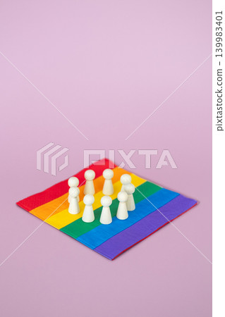 Group of wooden figurines stands in circle on rainbow pride flag against pink background. DEI Diversity, Equity, and Inclusion policy implementation, inclusive corporate culture, workplace equity. 139983401