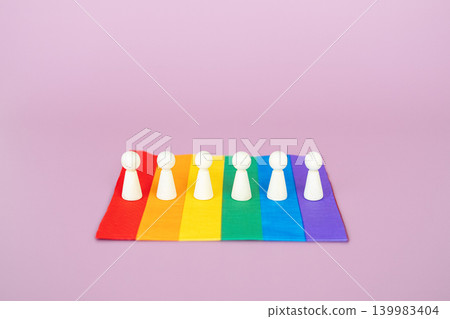 Wooden figurines stand in straight line on rainbow flag against purple background. World Pride 2026 theme, global LGBTQIA gathering, unity in diversity, amplify queer voices. Wooden figurines stand in straight line on rainbow flag against purple background. World Pride 2026 theme, global LGBTQIA gathering, unity in diversity, amplify queer voices. 139983404