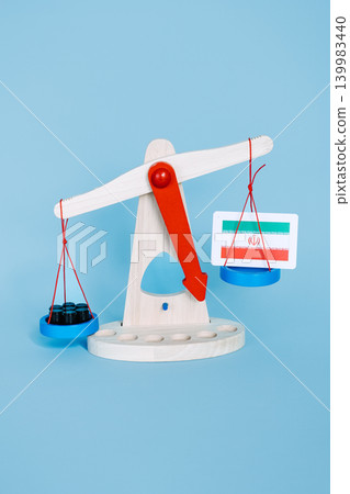 Wooden scales weighing small black barrels against Iranian flag on blue background. Iran oil sanctions, global trade embargo, economic pressure strategy. Wooden scales weighing small black barrels against Iranian flag on blue background. Iran oil sanctions, global trade embargo, economic pressure strategy. 139983440