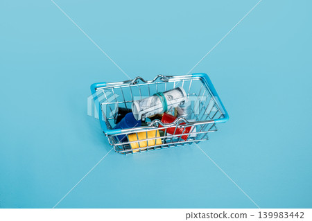 Small shopping basket contains rolled dollar bill resting on miniature oil drums. Economic recession impact, industrial resource consumption, energy market volatility. Small shopping basket contains rolled dollar bill resting on miniature oil drums. Economic recession impact, industrial resource consumption, energy market volatility. 139983442