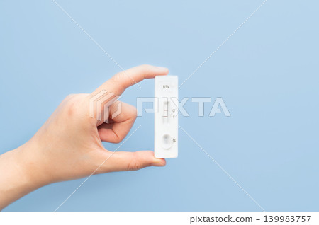 Woman hands holding Respiratory Syncytial Virus (RSV) antigen rapid test kit with positive result on blue background. Woman hands holding Respiratory Syncytial Virus (RSV) antigen rapid test kit with positive result on blue background. 139983757