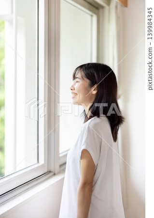 A young Japanese woman takes a deep breath by the window. A young Japanese woman takes a deep breath by the window. 139984345