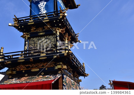 The Inuyama Festival in Aichi Prefecture, Japan: A magnificent procession of elaborate floats called "Kurumayama" and the keep of Inuyama Castle, under a sky full of blooming cherry blossoms. 139984361