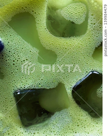 Close-up matcha foam with ice cubes shows bubbles, liquid surface, glass rim, and creamy green drink texture for menu design. Natural background for matcha menu, cafe branding, beverage content Close-up matcha foam with ice cubes shows bubbles, liquid surface, glass rim, and creamy green drink texture for menu design. Natural background for matcha menu, cafe branding, beverage content 139984479