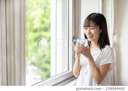 一位年輕的日本女子手捧一杯水，望著窗外。 139984492