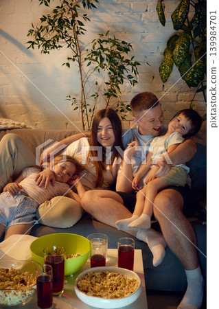 Happy family eating popcorn during home entertainment evening on sofa. Happy family eating popcorn during home entertainment evening on sofa. 139984701