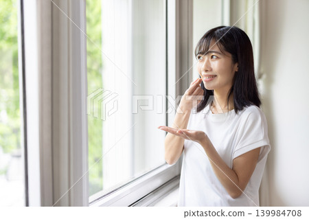 A young Japanese woman smiles by the window, holding a pill in her hand. 139984708