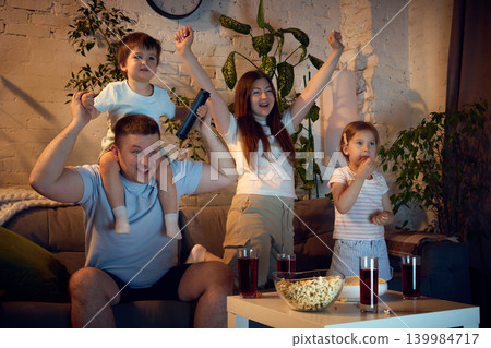 Family cheering while watching sports game together during cozy evening at home 139984717