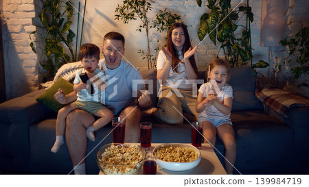 Happy parents and children applauding while watching television at home. 139984719