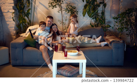 Parents and children relaxing on sofa during quiet movie evening. Parents and children relaxing on sofa during quiet movie evening. 139984722