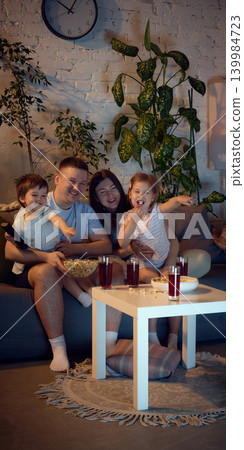 Family reacting to funny scene during movie night with snacks. Family reacting to funny scene during movie night with snacks. 139984723