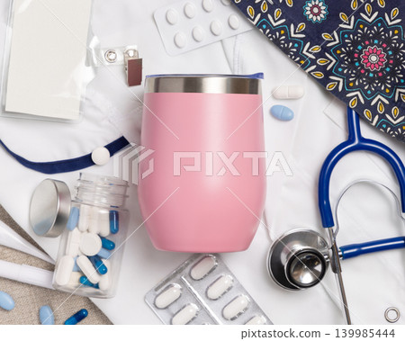 Pink 12 oz tumbler mockup with medical accessories and scrub uniform top view, blank template Pink 12 oz tumbler mockup with medical accessories and scrub uniform top view, blank template 139985444
