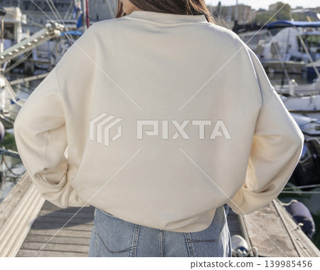 Blank beige oversized unisex sweatshirt mockup on woman near boats and yachts, back copy space Blank beige oversized unisex sweatshirt mockup on woman near boats and yachts, back copy space 139985456