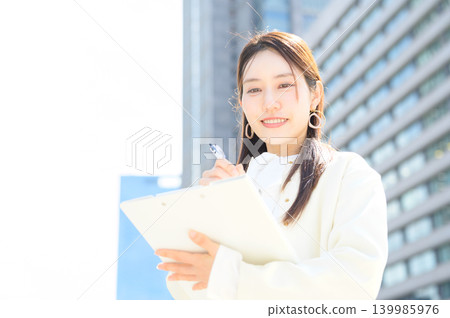 A Japanese businesswoman writing on a clipboard in an office district. A Japanese businesswoman writing on a clipboard in an office district. 139985976
