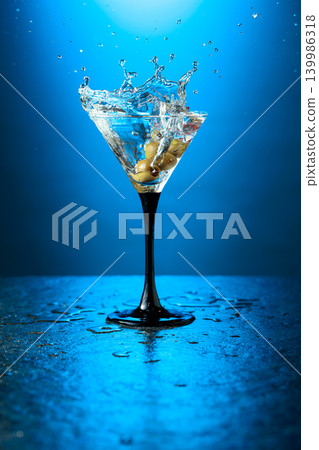 A green olives drops into a martini glass, creating a beautiful splash. 139986318