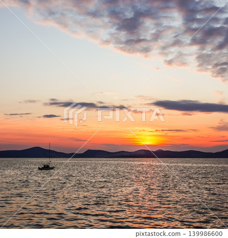 Calm evening sunset with a sailboat on the water, reflecting vibrant colors across the sky in Gulluk, Turkey Calm evening sunset with a sailboat on the water, reflecting vibrant colors across the sky in Gulluk, Turkey 139986600