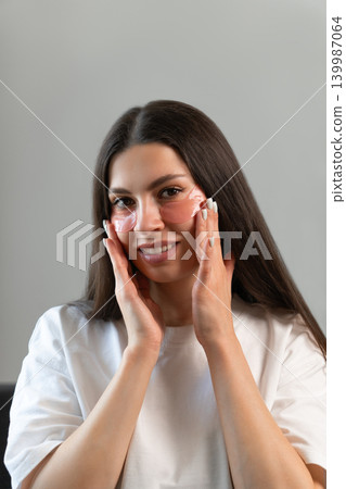 Vertical beauty portrait of young woman wearing hydrogel under-eye patches during skincare routine at home. Concept of self-care, healthy skin and modern facial treatment. Vertical beauty portrait of young woman wearing hydrogel under-eye patches during skincare routine at home. Concept of self-care, healthy skin and modern facial treatment. 139987064